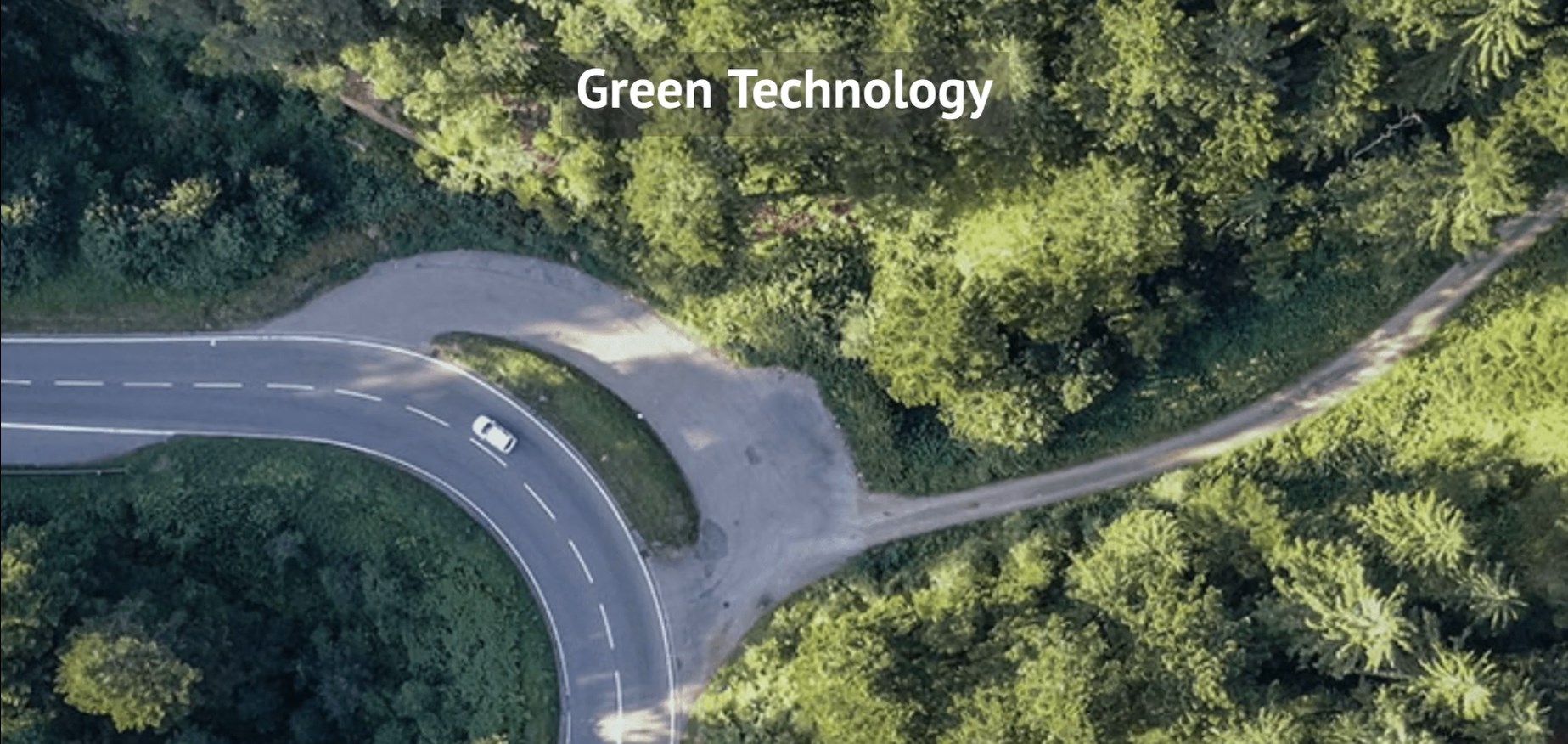 High overhead on car driving on road in woods with words "Green Technology" in white at top of the image