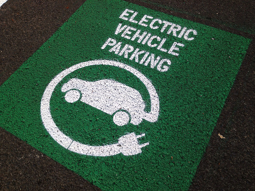 Green electric vehicle parking paint on asphalt in parking lot. Logo of a car with power cord coming out of it.