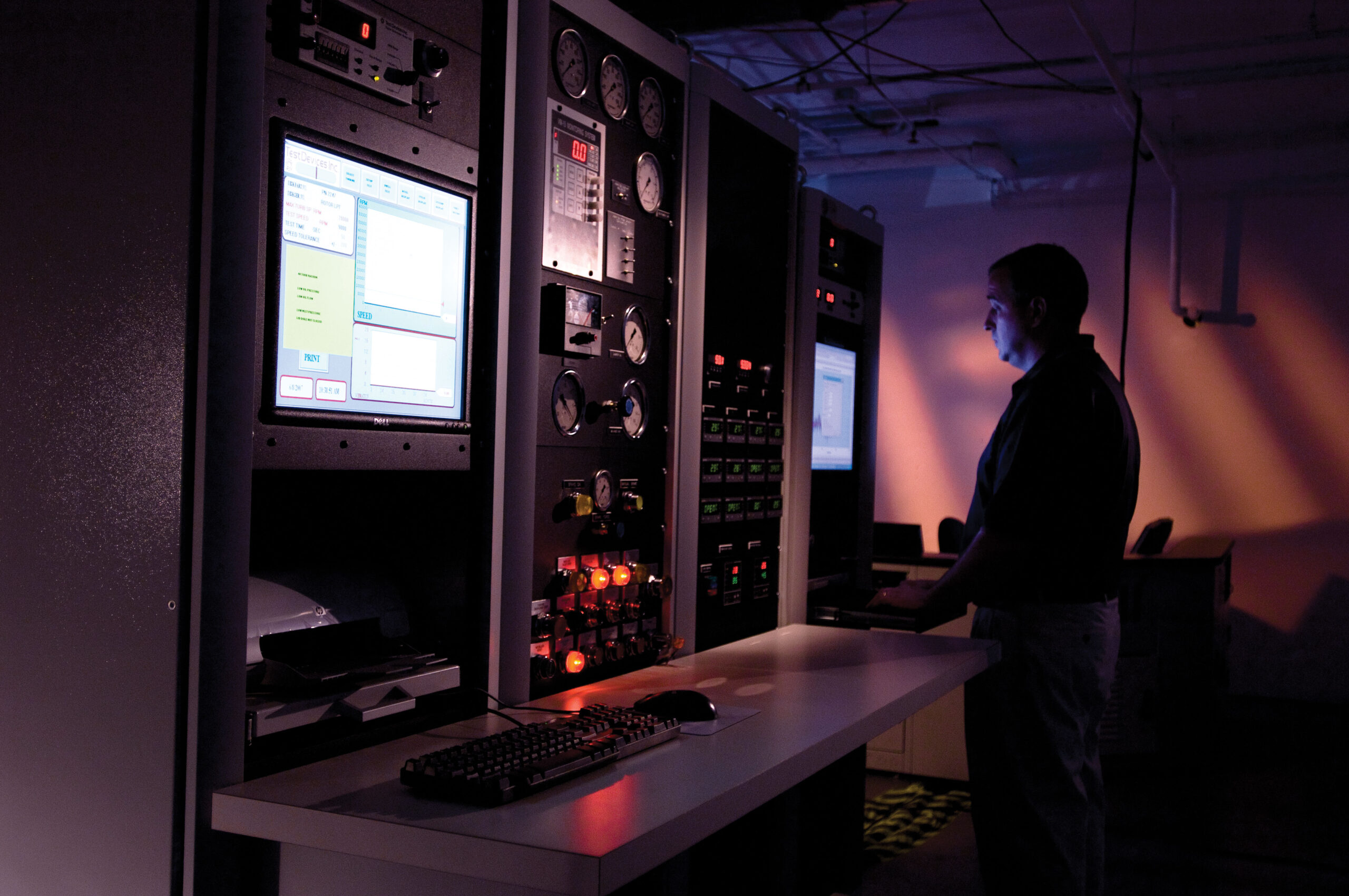 Engineer working in dark room reading results of spin or balance test on monitor